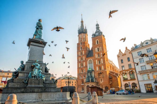 
 Old city center view with Adam Mickiewicz monument, St. Mary's Basilica and birds flying in Krakow on the morning